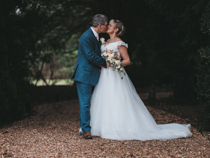 Stunning couple embracing with a kiss on their wedding day with the beautiful back drop of Holmewood Hall Cambridgeshire Bride and groom happy wedding candid wedding Holmewood hall Gayers Park Sopwell House St Albans Hunton Park Huntingdon 