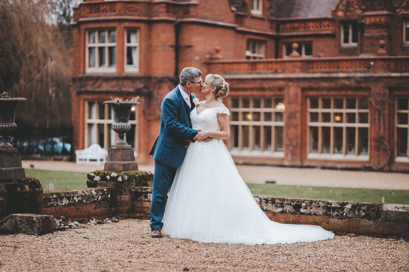Stunning couple embracing with a kiss on their wedding day with the beautiful back drop of Holmewood Hall Cambridgeshire 